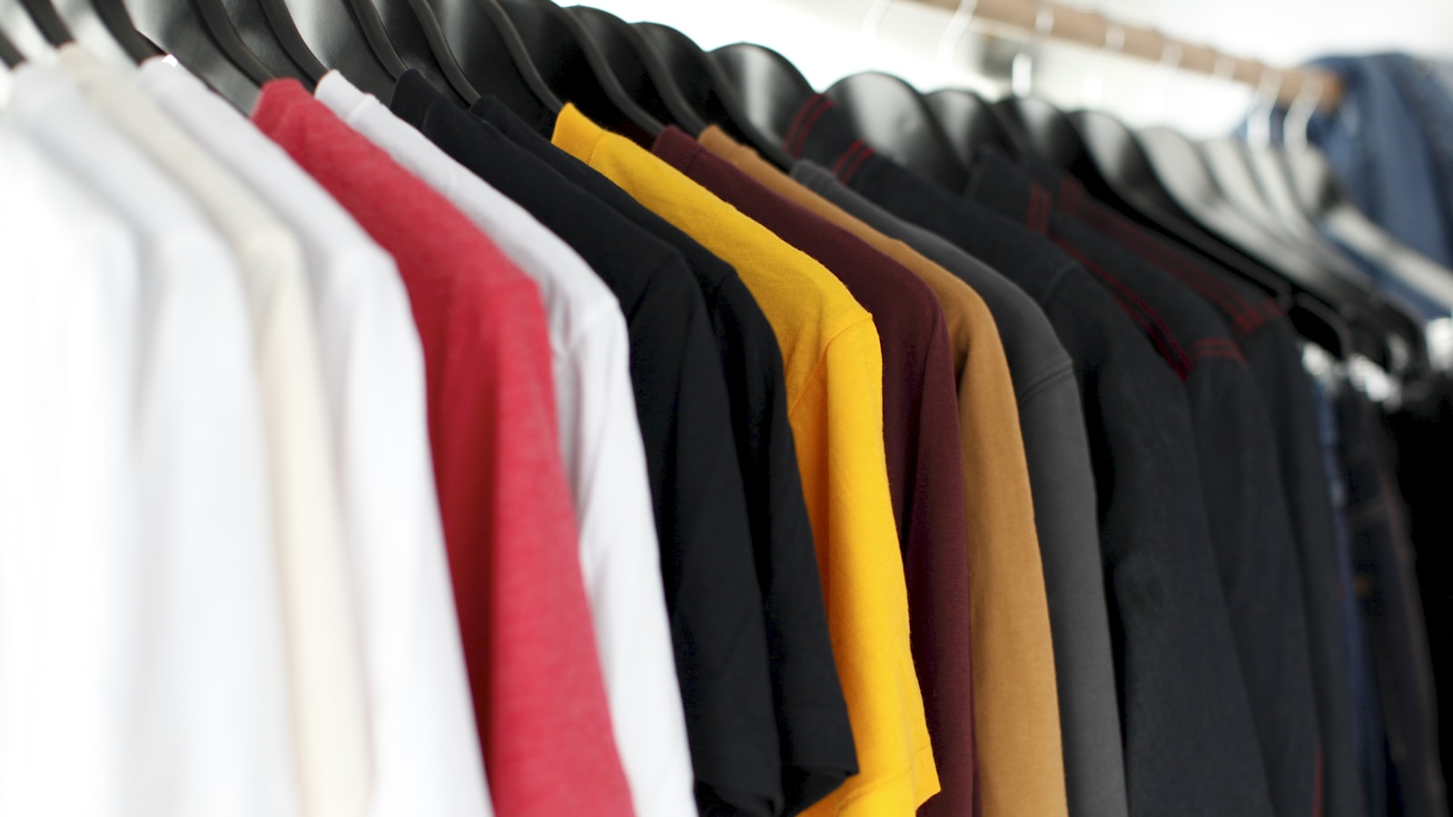 A neat rail of clothes in soft neutral colors hanging in an organized closet.