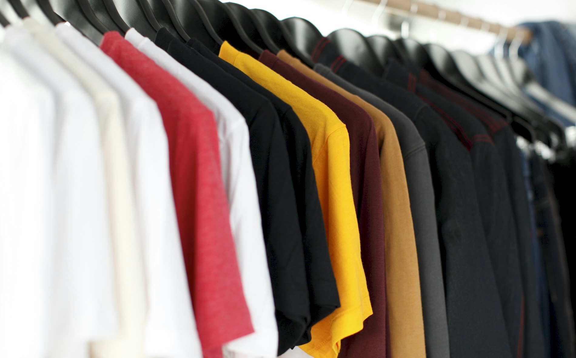 A neat rail of clothes in soft neutral colors hanging in an organized closet.