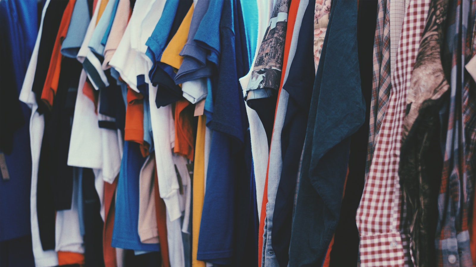 A rack of secondhand clothes on wooden hangers in a vintage shop.